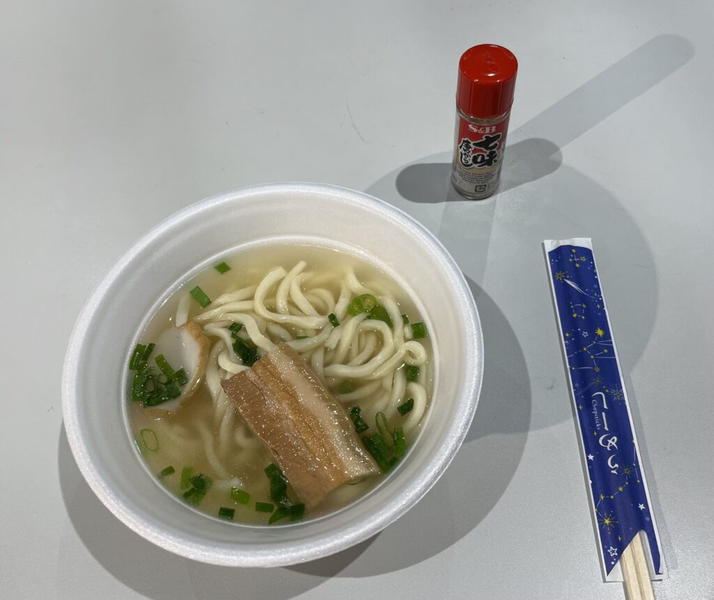 大東そば。プラスチックのおわんに太麺、三枚肉、かまぼこが載って青ネギを散りばめてます